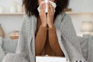 A woman wrapped up in a blanket sneezing into a tissue